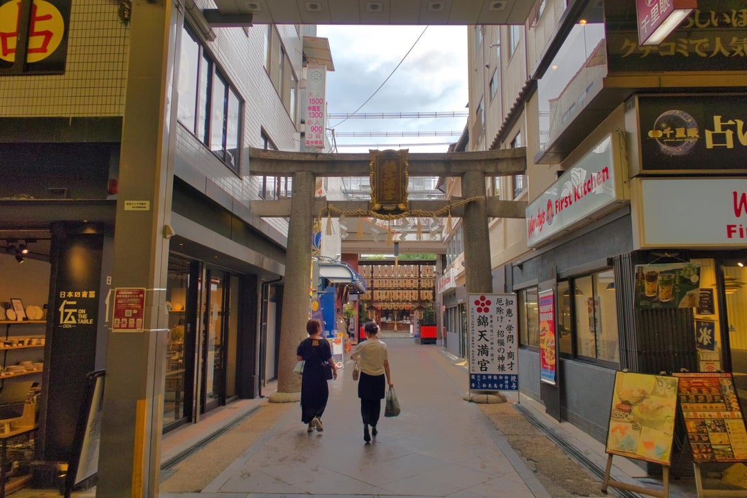 Nishiki Tenmangu Shrine is located at the eastern end of Nishiki-koji Street, where Kyoto's Nishiki Market is located. Its torii gate is pierced by buildings on both sides.